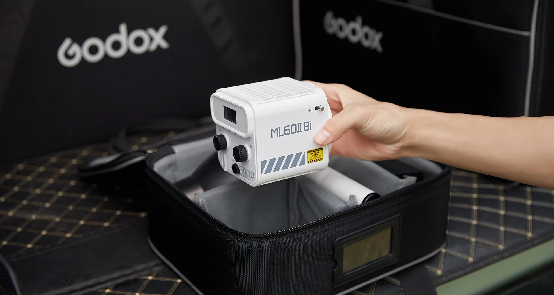 Компактний білий корпус моноблока Godox ML60II Bi в руці оператора над відкритим транспортувальним кейсом з ручкою та рефлектором